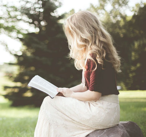 The Healed Soul – E-Book über Manifestation 2 Blonde Frau sitzt im Park und liest ein Buch, Natur im Hintergrund