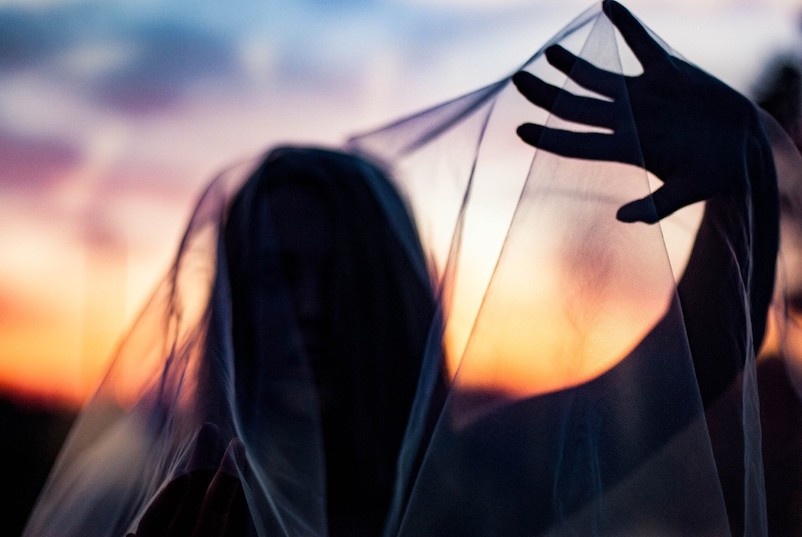 Silhouette einer Frau mit fließendem Tuch gegen Sonnenuntergang, energetische Aura