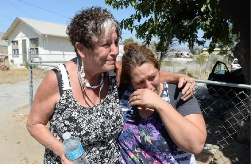 Zwei Frauen umarmen sich emotiona vor einem Haus, eine hält eine Wasserflasche