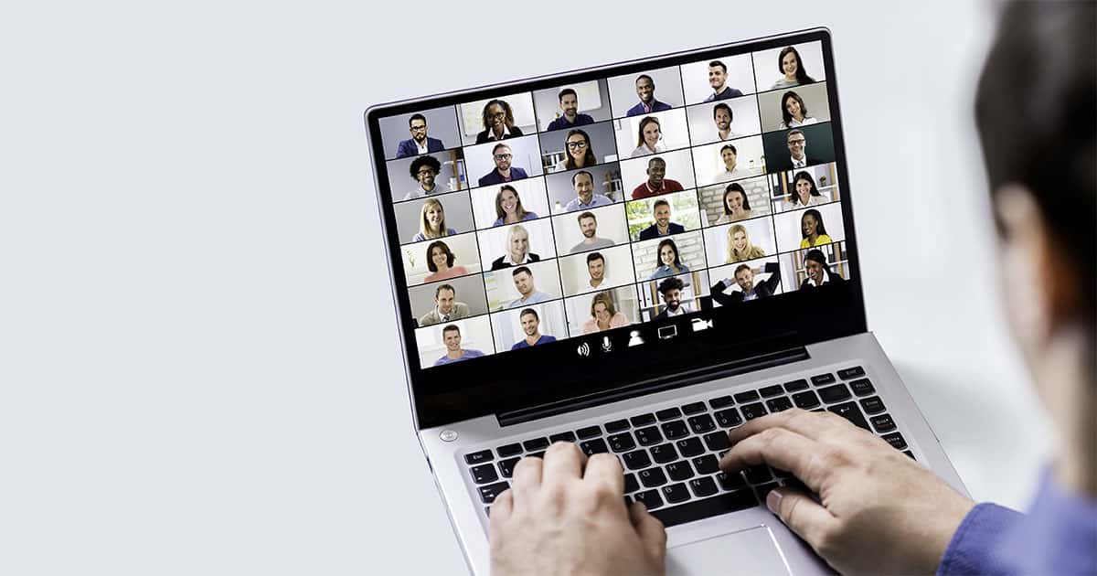 Laptop-Bildschirm mit Video-Konferenz von etwa 40 Personen in Grid-Layout, Hände auf Tastatur