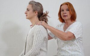 Praktische Anwendung: Therapeutin behandelt Klientin von hinten an der Schulter