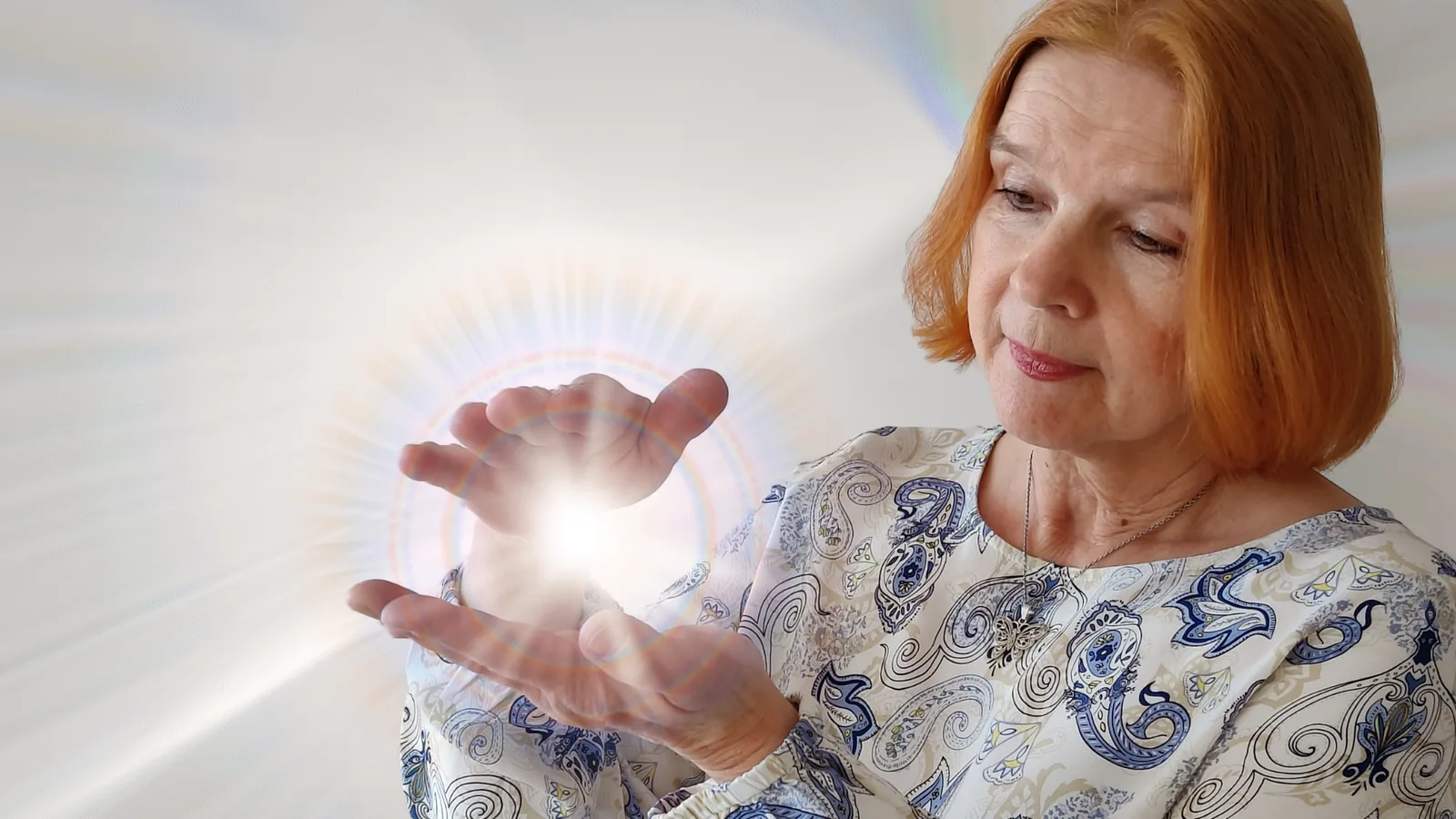 Frau mit rötlichen Haaren hält leuchtende Energiekugel in beiden Händen