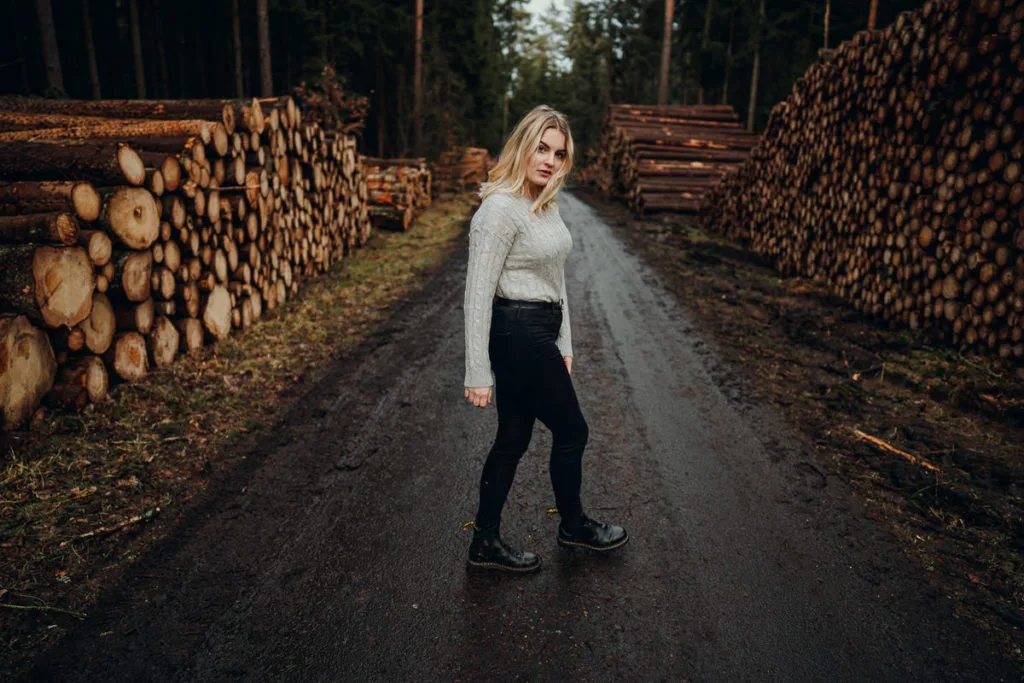 Blonde Frau in Waldweg zwischen Holzstapeln mit moody Farbbearbeitung