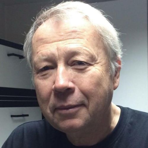 Porträt von Dirk Schrader, älterer Mann mit weißem Haar vor grauem Hintergrund