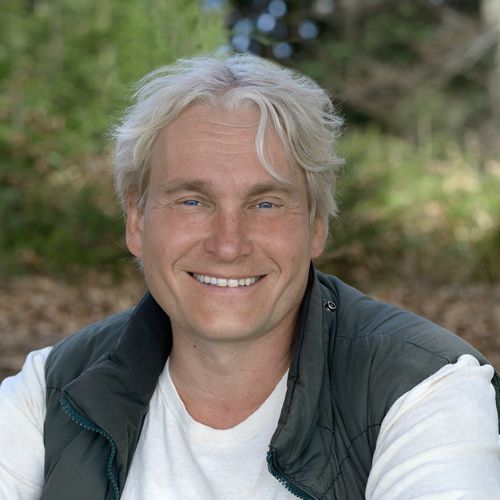 Porträt von Uwe Albrecht mit weißem Haar vor grünem Naturhintergrund