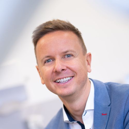 Porträt von Dr. Alexander Neubauer in blauem Blazer vor unscharfem Hintergrund