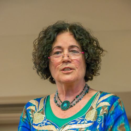 Porträt von Dr. Rosina Sonnenschmidt mit Brille und buntem Oberteil vor beigem Hintergrund