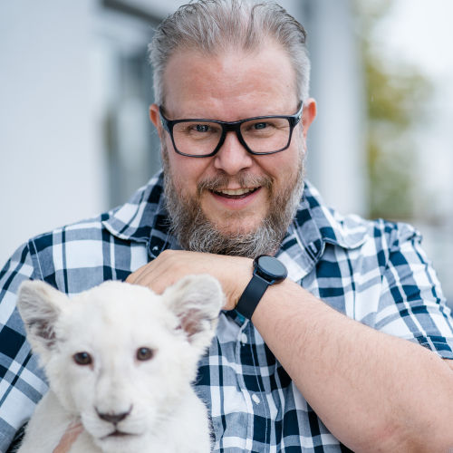 Tierarzt Henning Wilts mit Brille und kariertem Hemd neben weißem Hund, freundliches Porträt