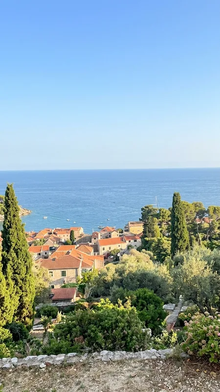 Luftaufnahme mediterraner Küstenort mit Häusern Zypressenbaumen und blauem Meer