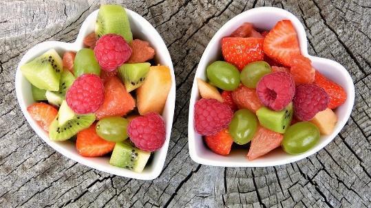 Zwei herzförmige Schüsseln mit Früchten auf Holzoberfläche, enthält Kiwi, Erdbeeren und Himbeeren