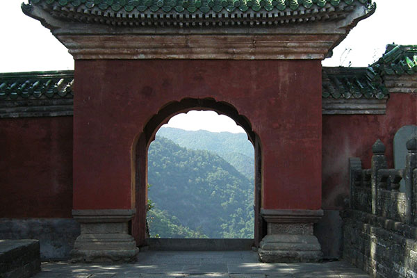 Traditionelles rotes Tor mit rundem Durchgang in einem chinesischen Tempel, Bergblick im Hintergrund