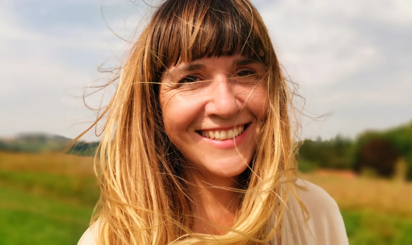 Trading Breathwork – Atem-Videokurs für Trader von Corrina Holzner 3 Corrina Holzner Porträt lächelnd auf Naturhintergrund mit Feldern und Himmel