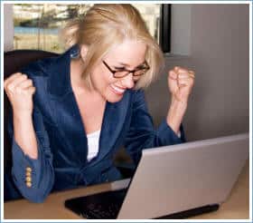 Frau mit Brille sitzt am Laptop und zeigt Siegesgeist