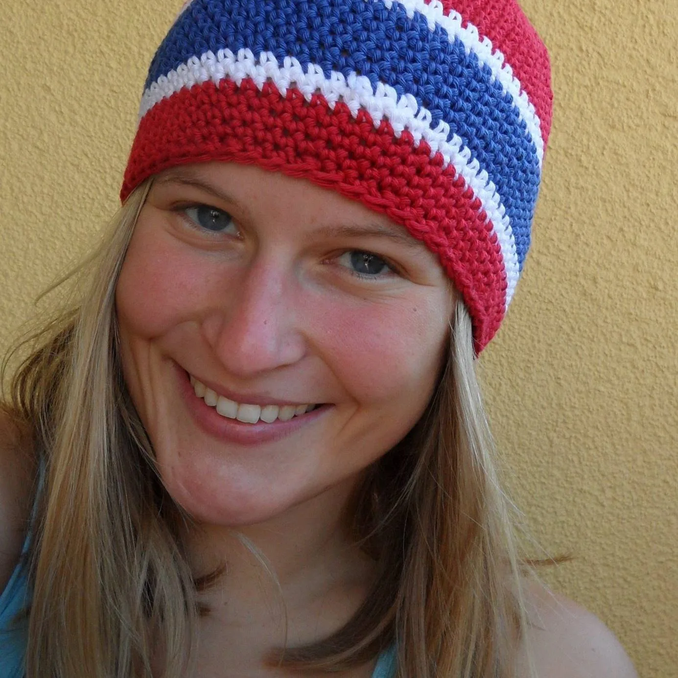 Lena lächelnde Frau mit farbigem Beanie-Mütze auf gelbem Hintergrund