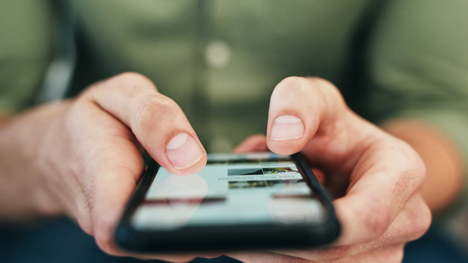 Hände halten Smartphone mit Social-Media-Feed in grüner Outdoor-Umgebung