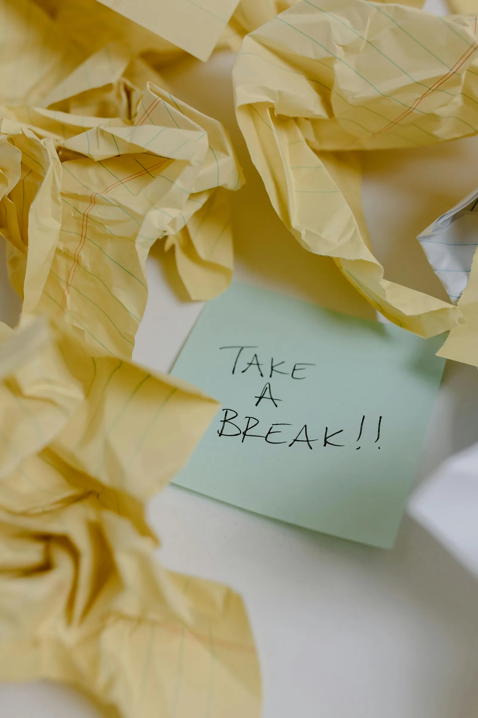 Grüner Notizzettel mit handschriftlichem Text "TAKE A BREAK!!" zwischen Papierknüllchen