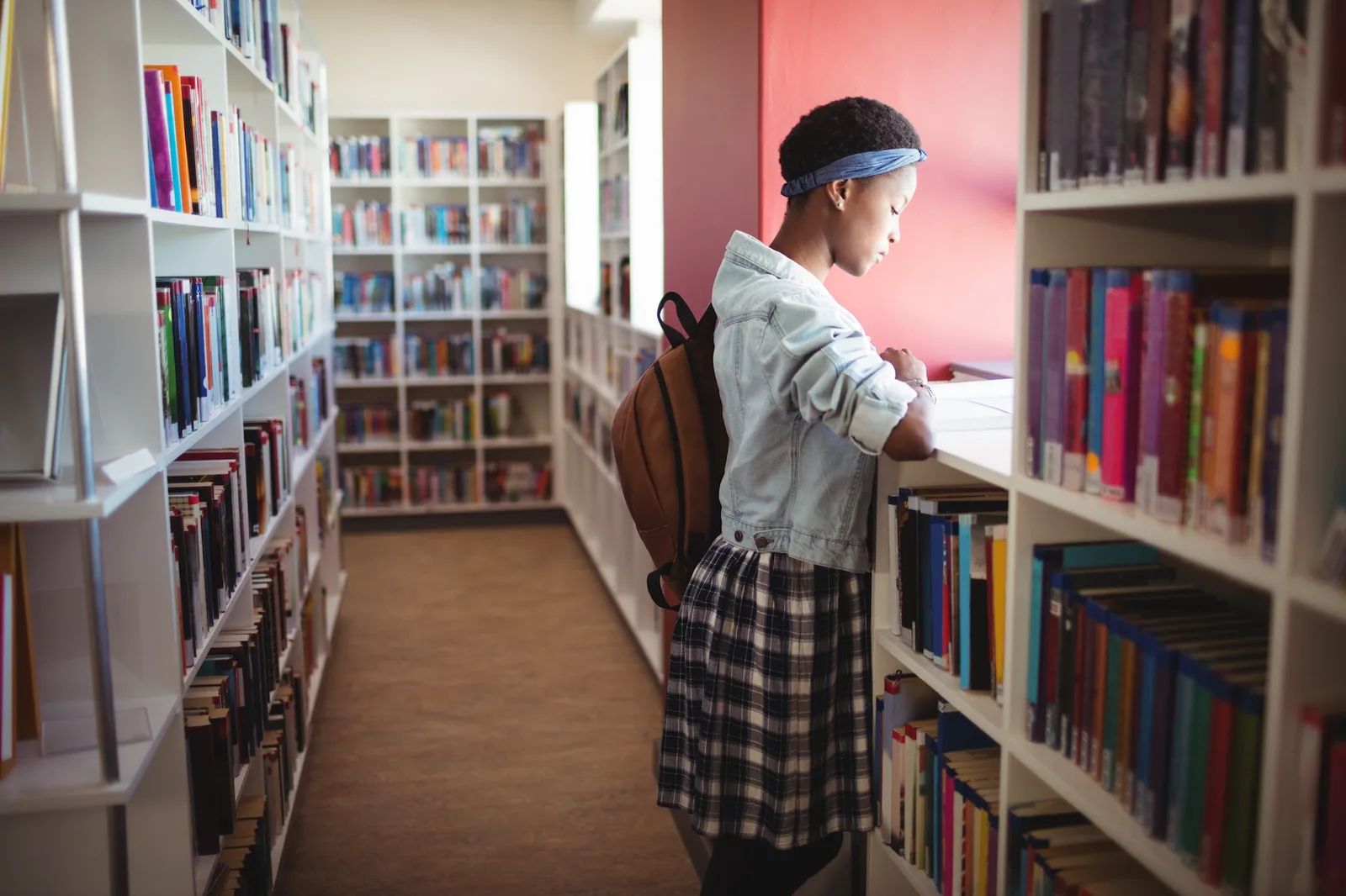 Und immer wieder aufstehen – E-Book über Krisenbewältigung 5 Schülerin mit Stirnband steht in Bibliothek zwischen Bücherregalen mit Rucksack