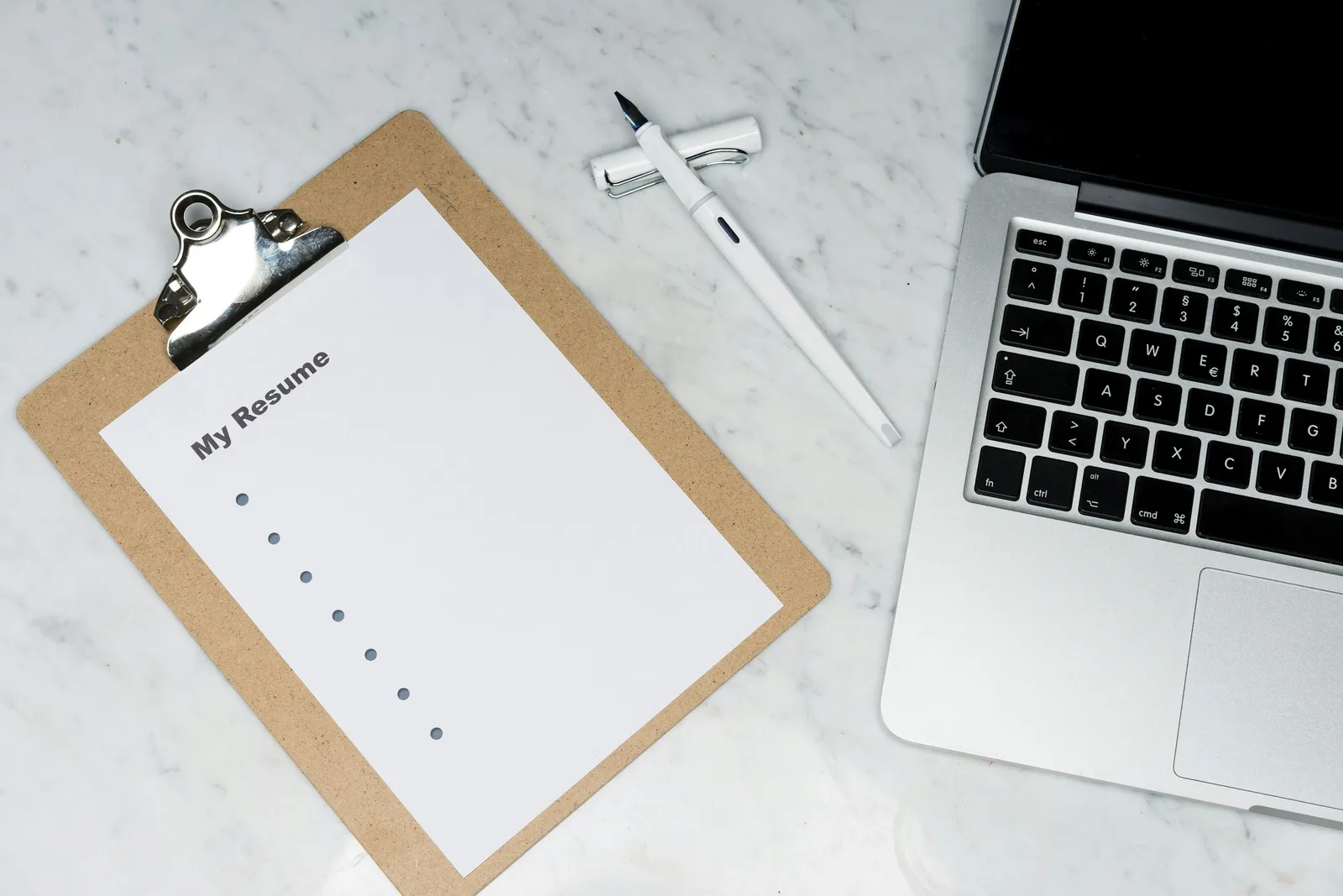 Laptop und Clipboard mit Resume Dokument auf Marmor-Schreibtisch