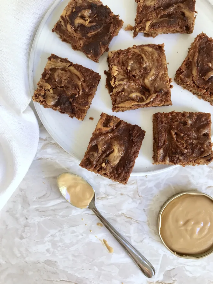 Süßkartoffel Brownies mit Erdnuss Swirl auf weißem Teller, daneben Schälchen mit Erdnusscreme