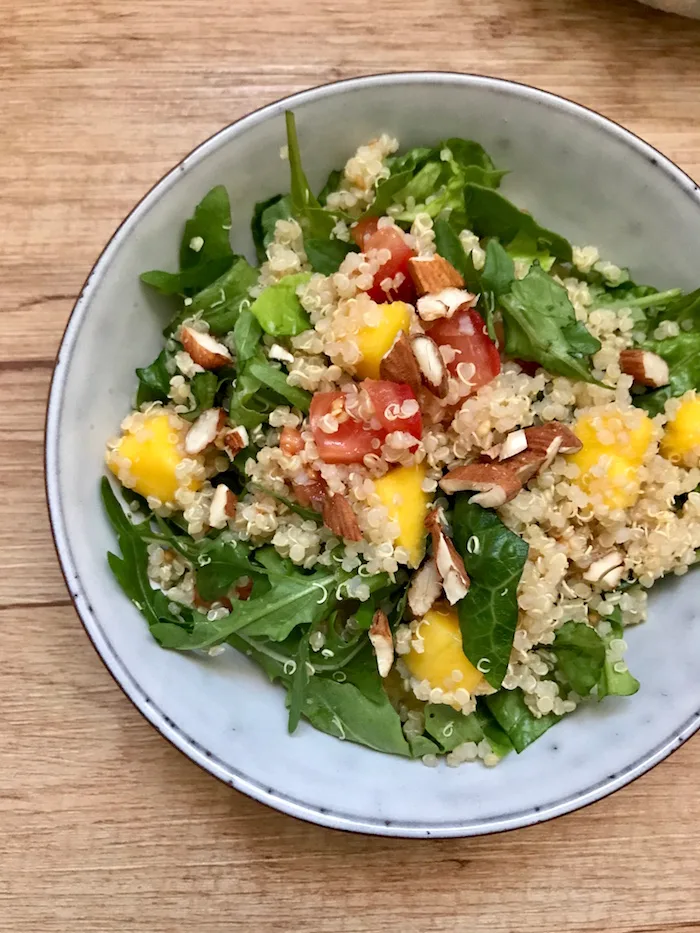 Vollwertiger Quinoa-Mango-Salat in grauer Schale mit grünem Blattgemüse, Quinoa, Mango und Nüssen