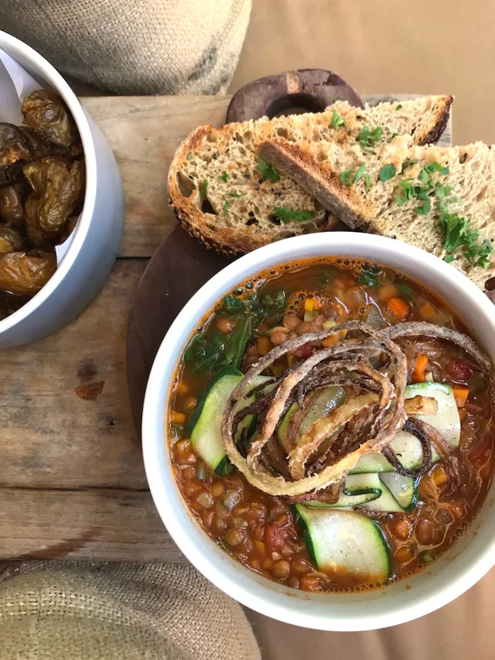 Vegane Linsensuppe in weißer Schale mit Brokkoli und Gemüse, Brot und Oliven daneben