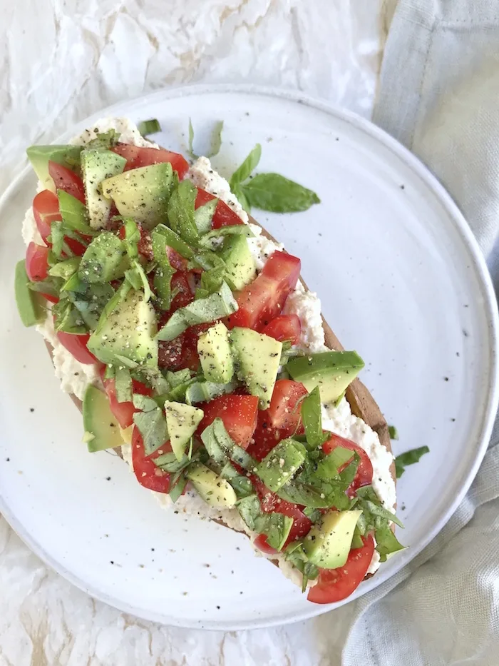 Gebackene Süßkartoffeln auf weißem Teller mit Cashew-Creme und Avocado-Tomaten-Mix