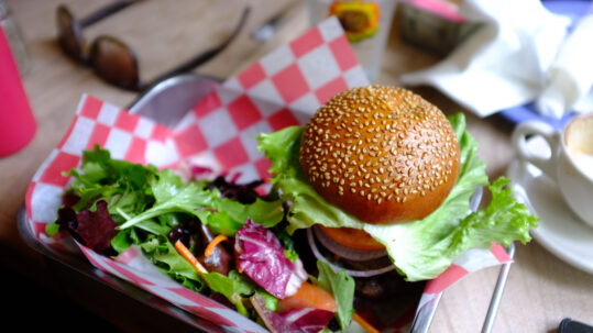 Vegetarischer Burger mit Sesambrötchen, Salat und roten Zwiebeln auf rosa Papier