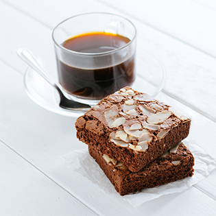 Raw Almond Brownies gestapelt neben Kaffeetasse, mit Mandeln belegt