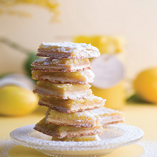 Lemon Bars gestapelt mit Puderzucker, Zitronen im Hintergrund
