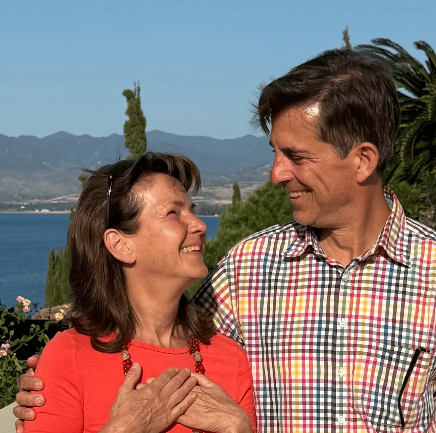 Paar Jens und Simone am Meer mit Gebirgen im Hintergrund, beide lächelnd