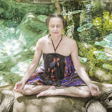 Frau Karin Lochner in Yogahaltung auf Stein mit naturgrünem Hintergrund