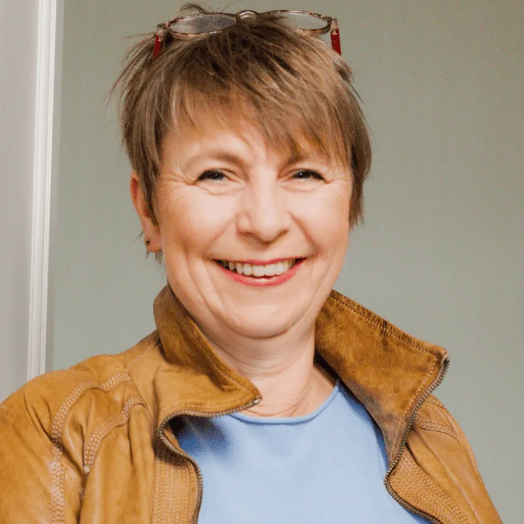 Porträt von Sylke Rohloff mit kurzen Haaren, Brille und brauner Jacke