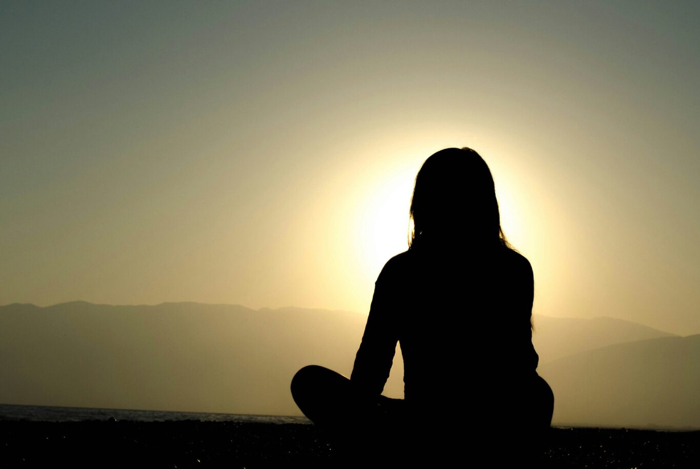 Silhouette einer sitzenden Frau vor Sonnenaufgang mit Berglandschaft im Hintergrund