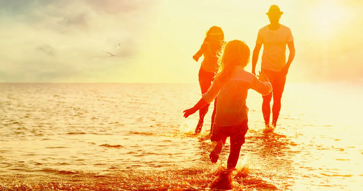 Familie mit zwei Kindern und Erwachsenem in leuchtend orangener Silhouette am Strand bei Sonnenaufgang