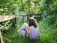 Zwei Kinder sitzen mit Hund im grünen Garten, von hinten fotografiert