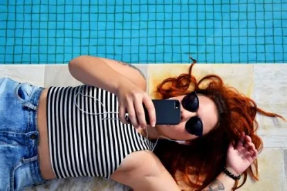 Frau mit roten Locken und Sonnenbrille entspannt am Pool neben Wasser