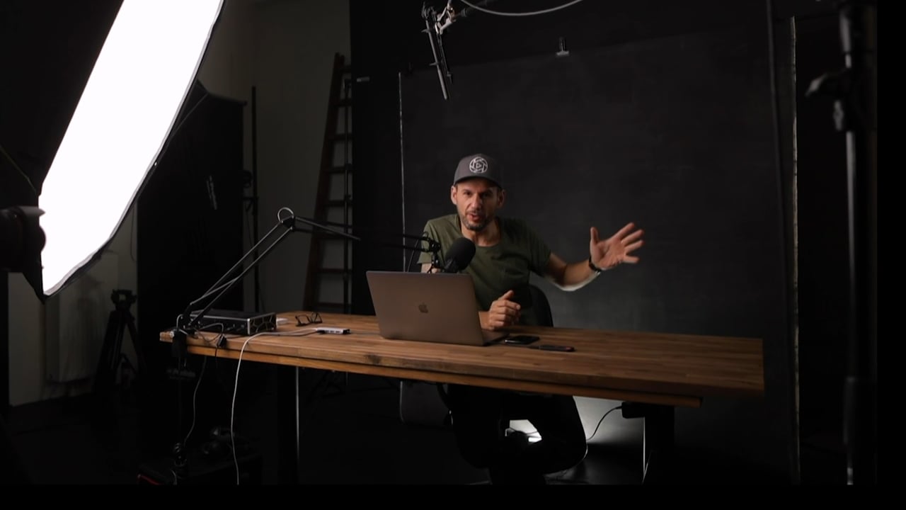 Visual Storytelling – Videokurs fürs Filmen von Christian Anderl 3 Christian Anderl sitzt am Holztisch vor Laptop im professionellen Videostudio mit Ringlight und Mikrofonaufbau