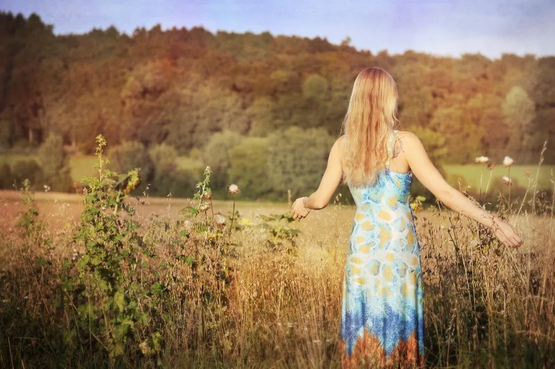 Frau in buntem Kleid steht in Herbstlandschaft mit Wald im Hintergrund