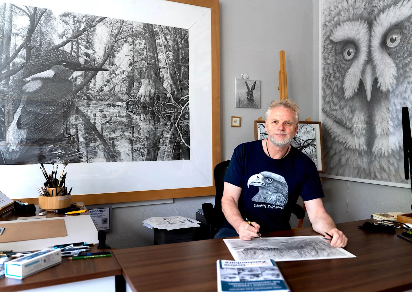 Ralf Wilhelm Schmidt Zeichner im Atelier mit Zeichnungen an der Wand und Werkzeugen am Schreibtisch