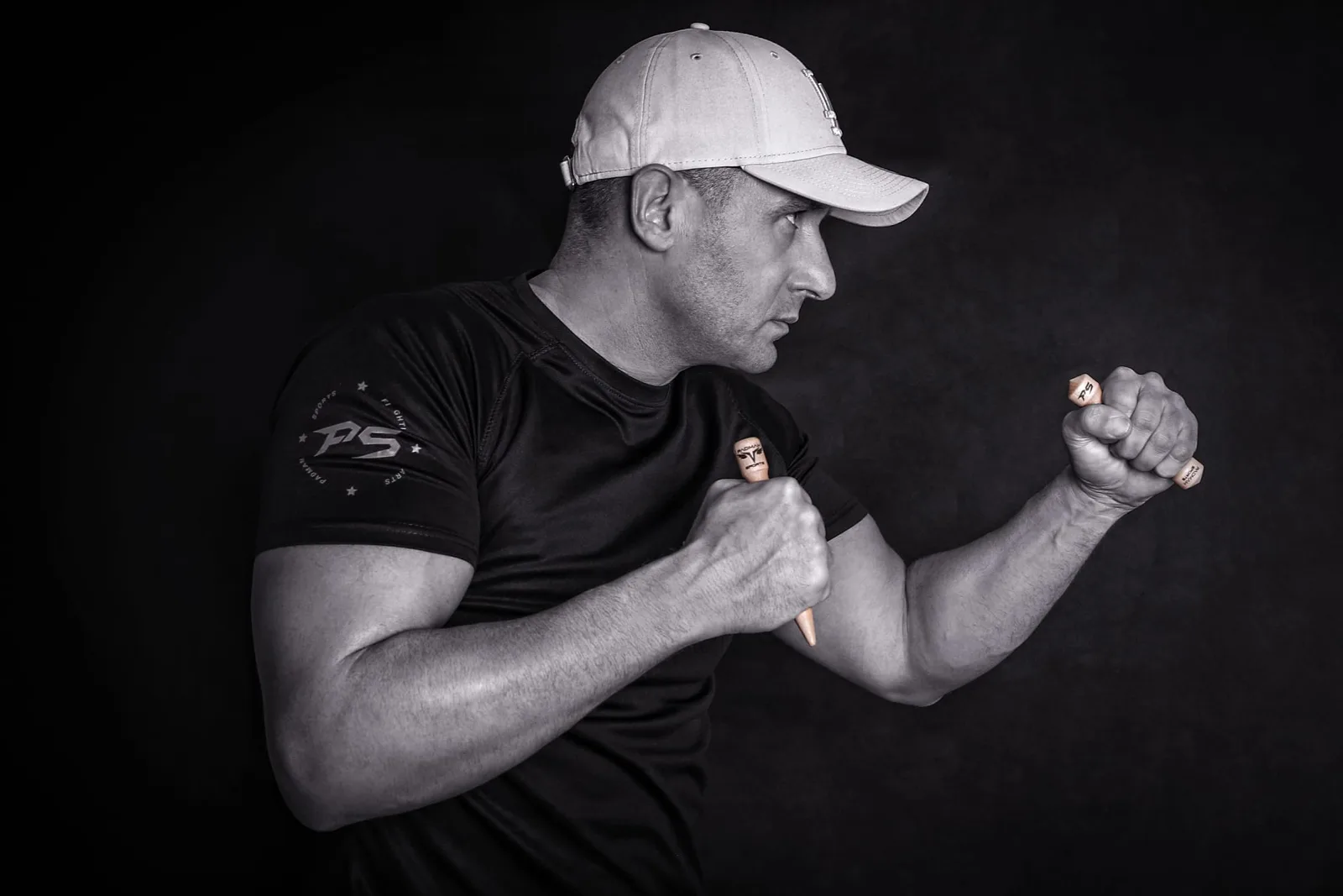Mann in schwarzem PS-Shirt und weißer Cap demonstriert Kampfhaltung mit Trainings-Gadgets