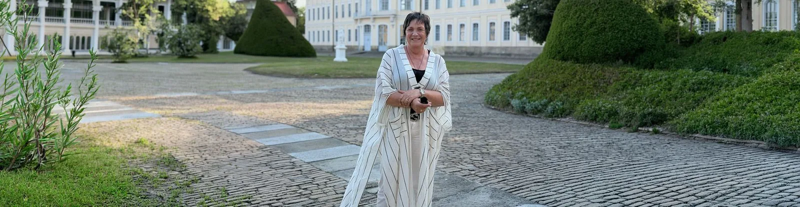Porträt von Steffi Christian in beiger Leinenjacke in klassischer Parkanlage