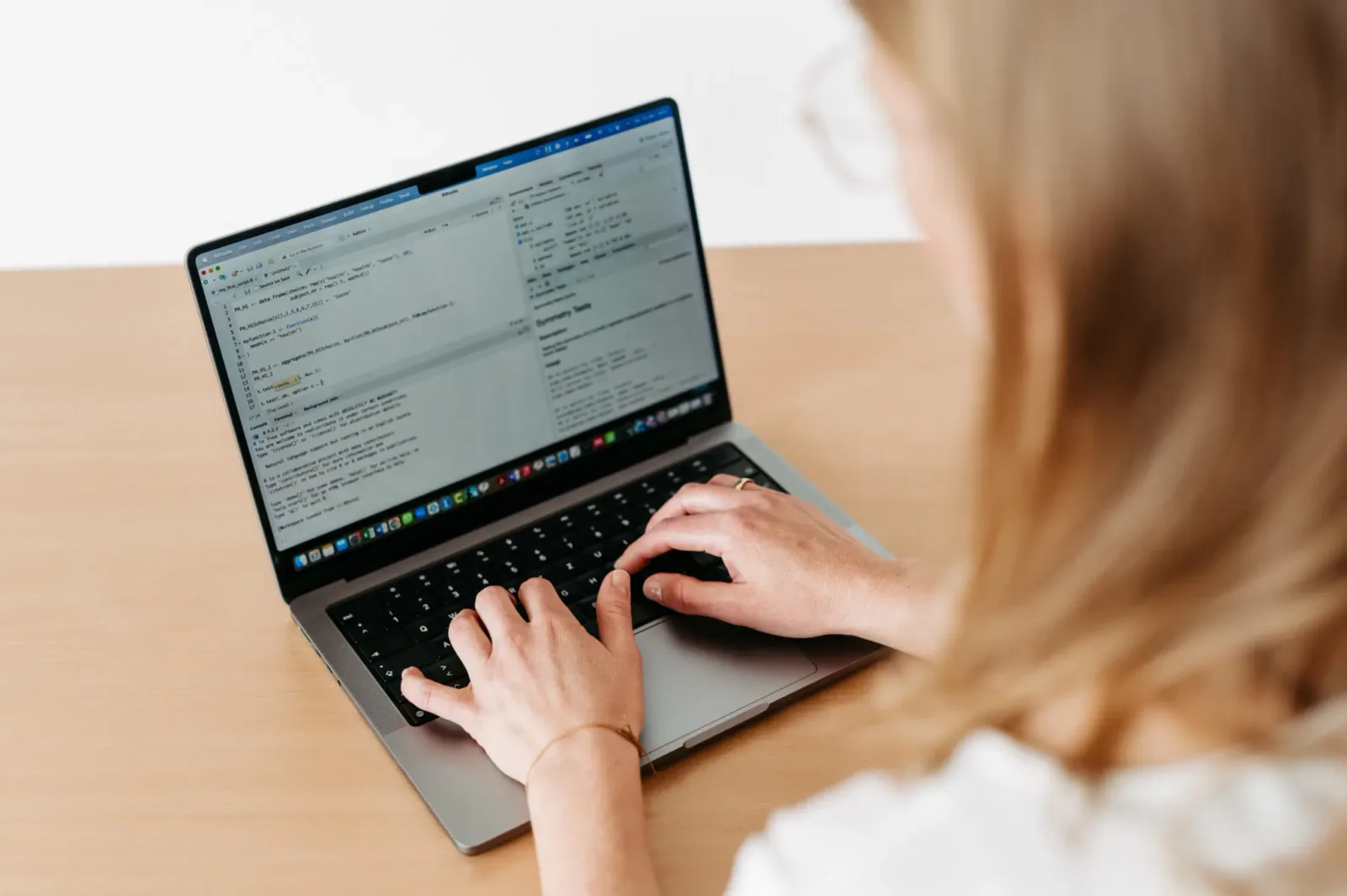 Frau von hinten mit Brille arbeitet konzentriert an Laptop mit Code auf dem Bildschirm