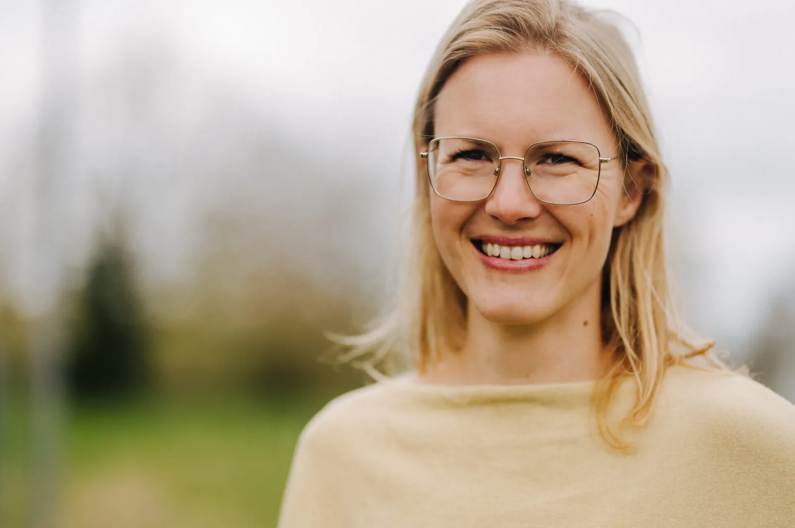 Daniela Keller trägt hellgelbes Shirt, lächelt mit Brille vor unscharfem grünem Hintergrund