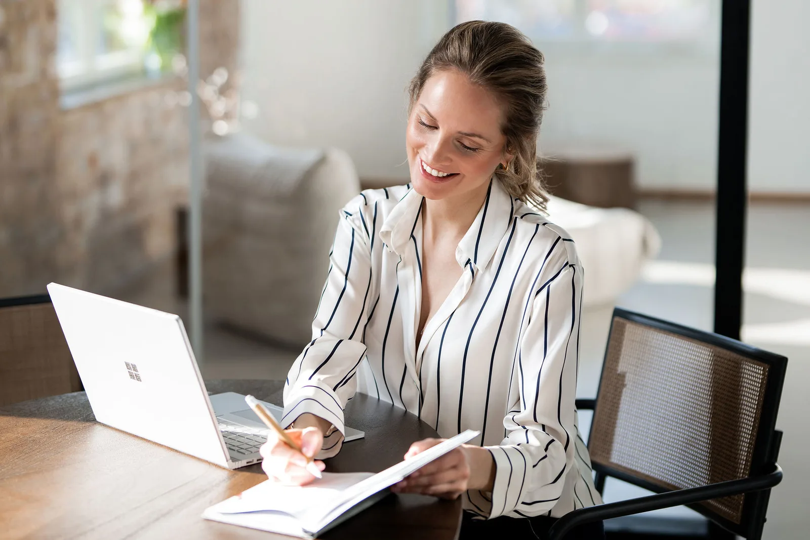 Frau in Businesskleidung sitzt am Schreibtisch und arbeitet lächelnd am Laptop