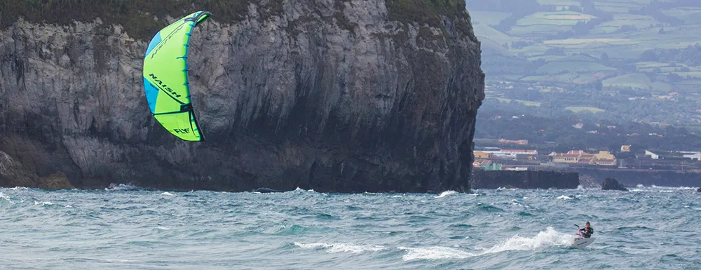 Kitesurfen mit grünem Kite vor Felsklippe auf den Azoren