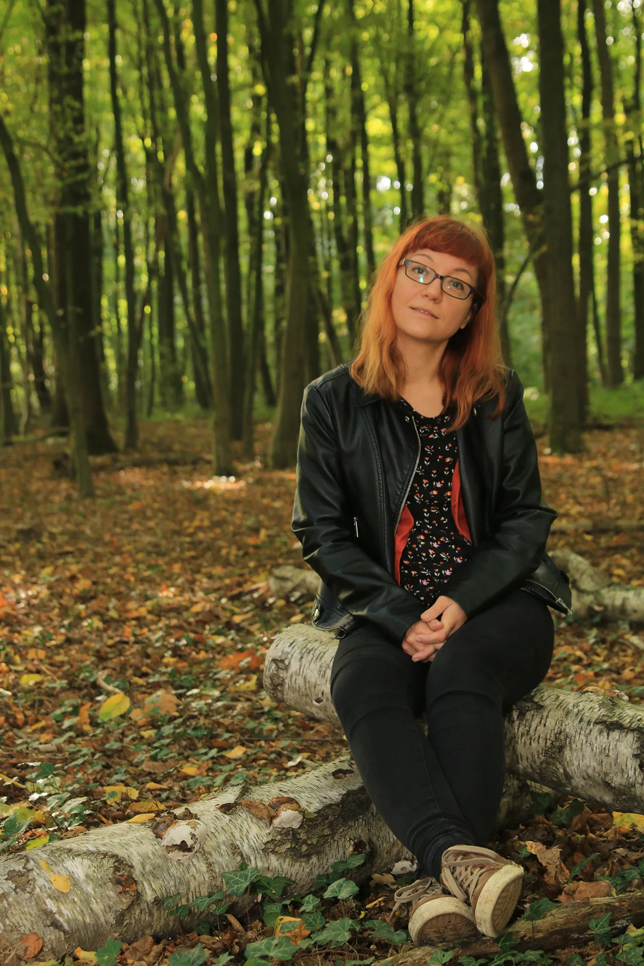 Porträt einer Frau mit roten Haaren und Brille in einem Birkenwald sitzend