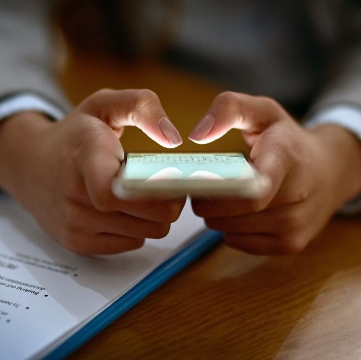 Kinderhände halten leuchtendes Smartphone über Blatt Papier, Detailaufnahme