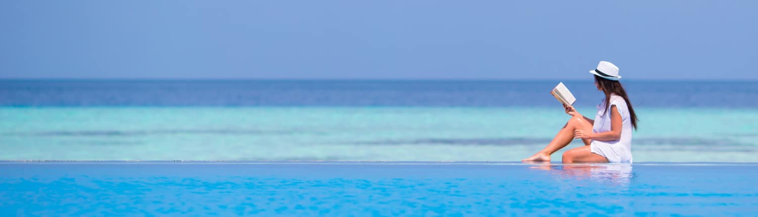 Wasser – E-Book für mehr Vitalität 3 Frau in weißem Kleid und Hut sitzt im flachen Wasser am Strand, liest Buch