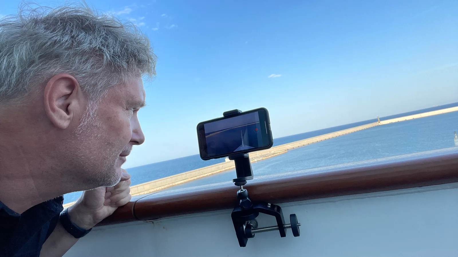 Wayne Morris – Musikprogramm für Kreuzfahrten 1 Mann mit grauem Haar filmt das Meer mit iPhone auf Smartphone-Halter an Schiffsreling
