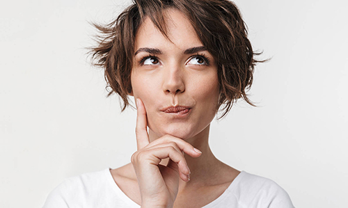 Frau mit kurzen braunen Haaren in nachdenklicher Pose mit Hand am Kinn
